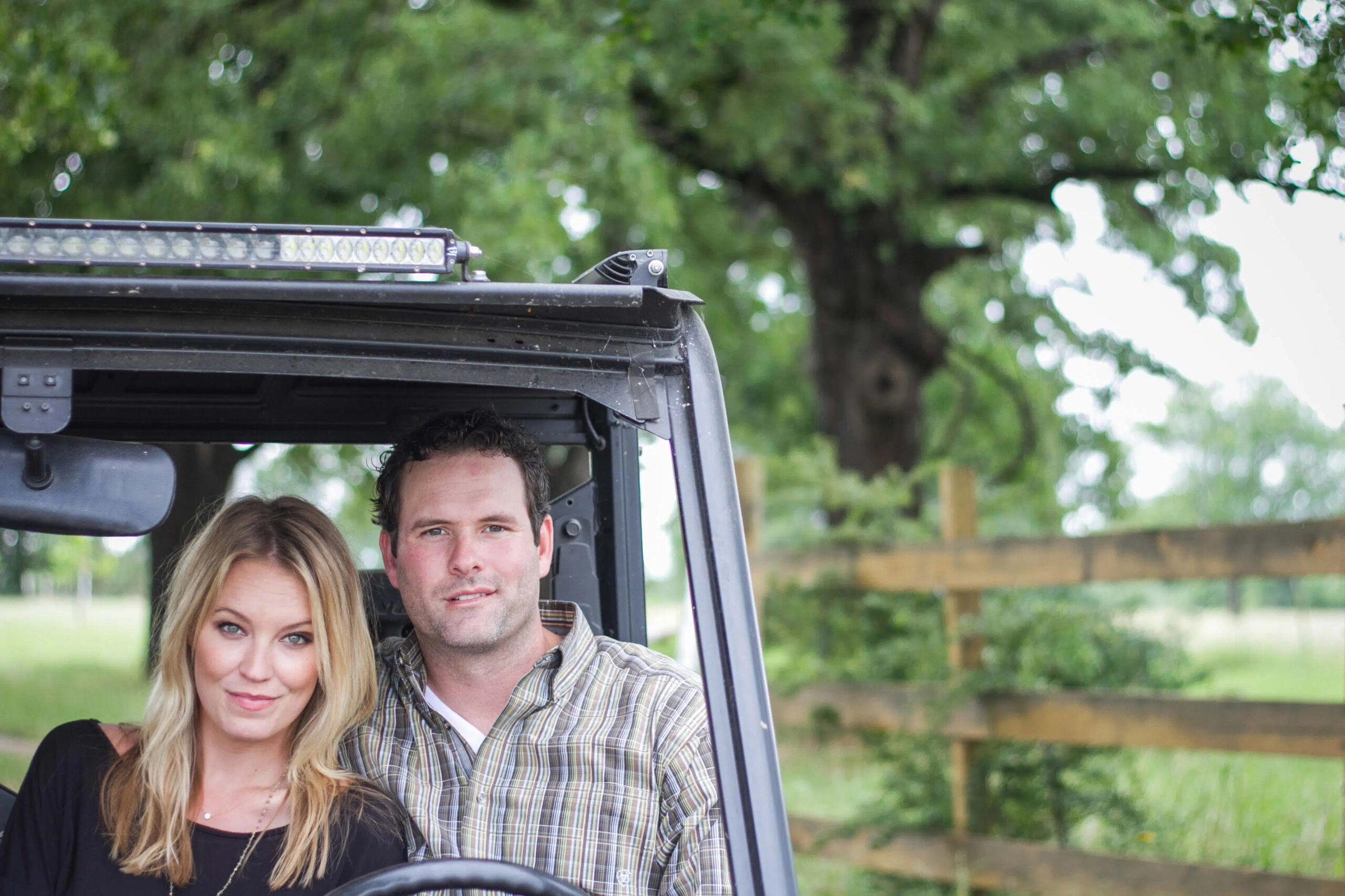 Man and woman pose outdoors inside of a vehicle
