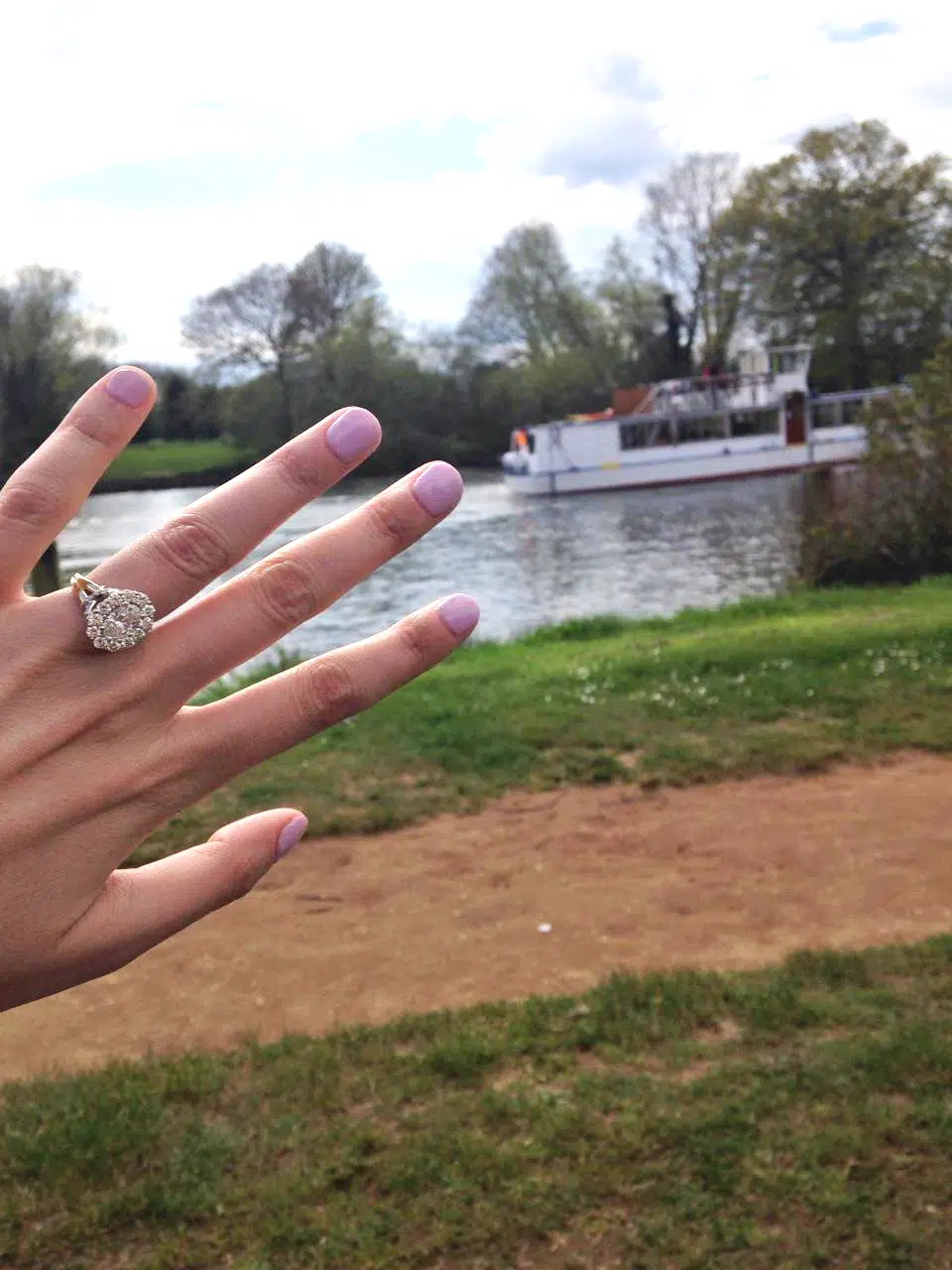 Woman holds up her engagement ring in front of a pond in a park