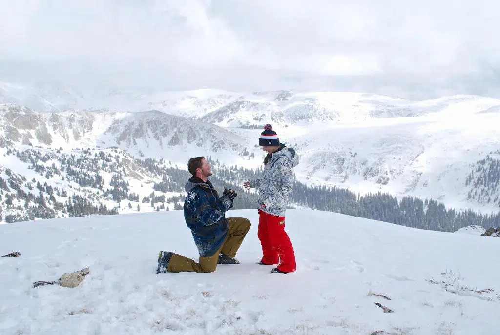 Man proposes to woman on a snowy mountaintop