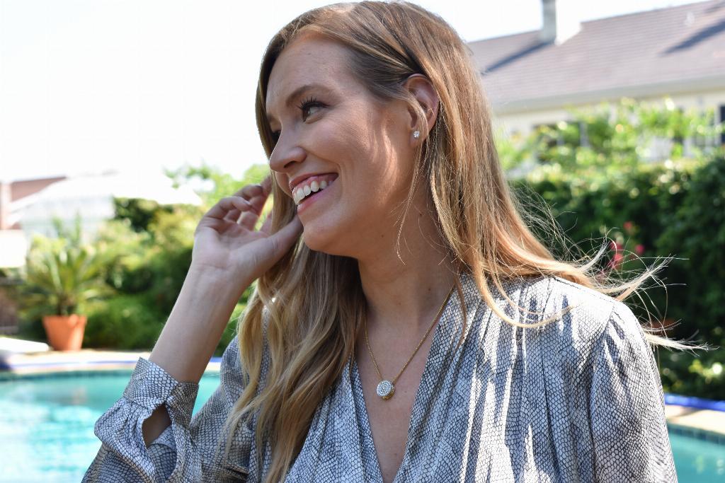 Woman holds her hand next to her face showing off jewelry, in front of a pool