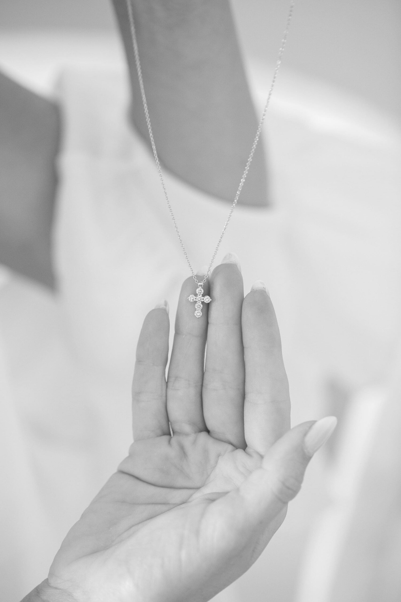 Cross shaped necklace being held, black and white