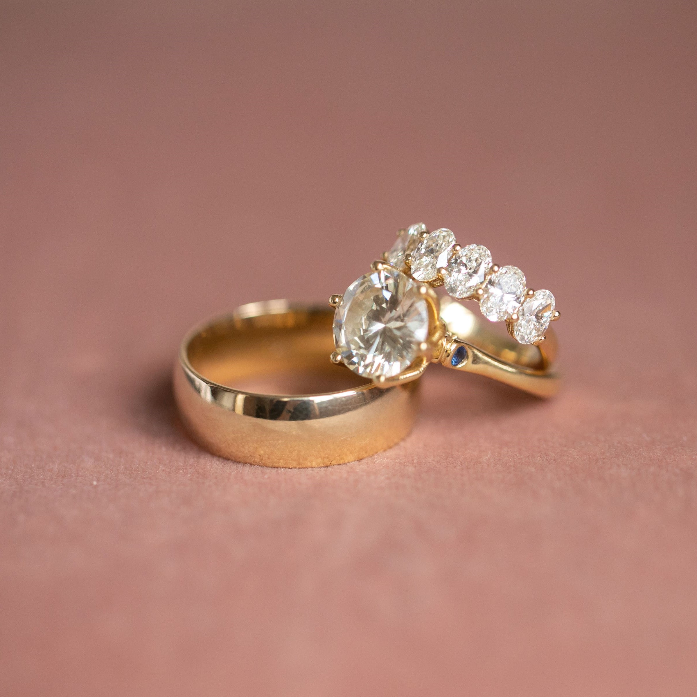 Gold wedding rings stacked atop a pink backdrop