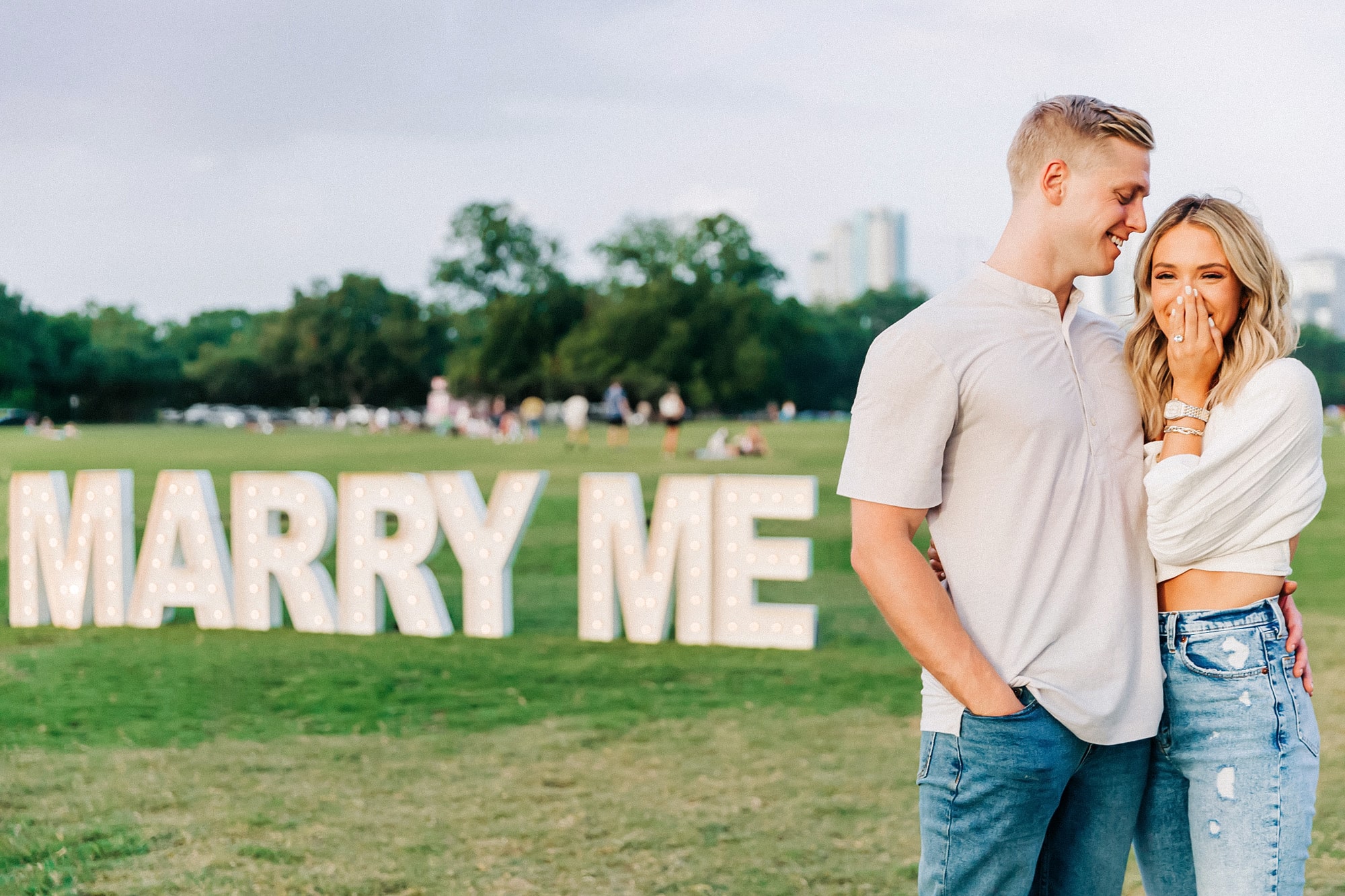 Lee and Emily standing in front of a marry me sign