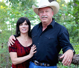 Man and woman embraced, pose for a photo with a wooded backdrop