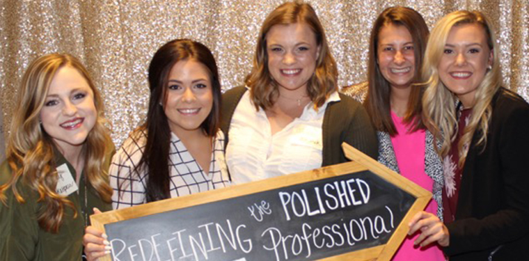 Women posing, holding a sign that says 'redefining the polished professional'