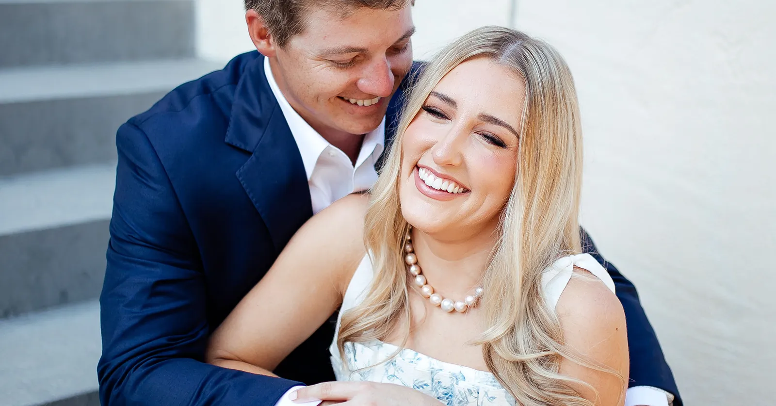 Man in blue suite and woman in white dress and pearl jewelry