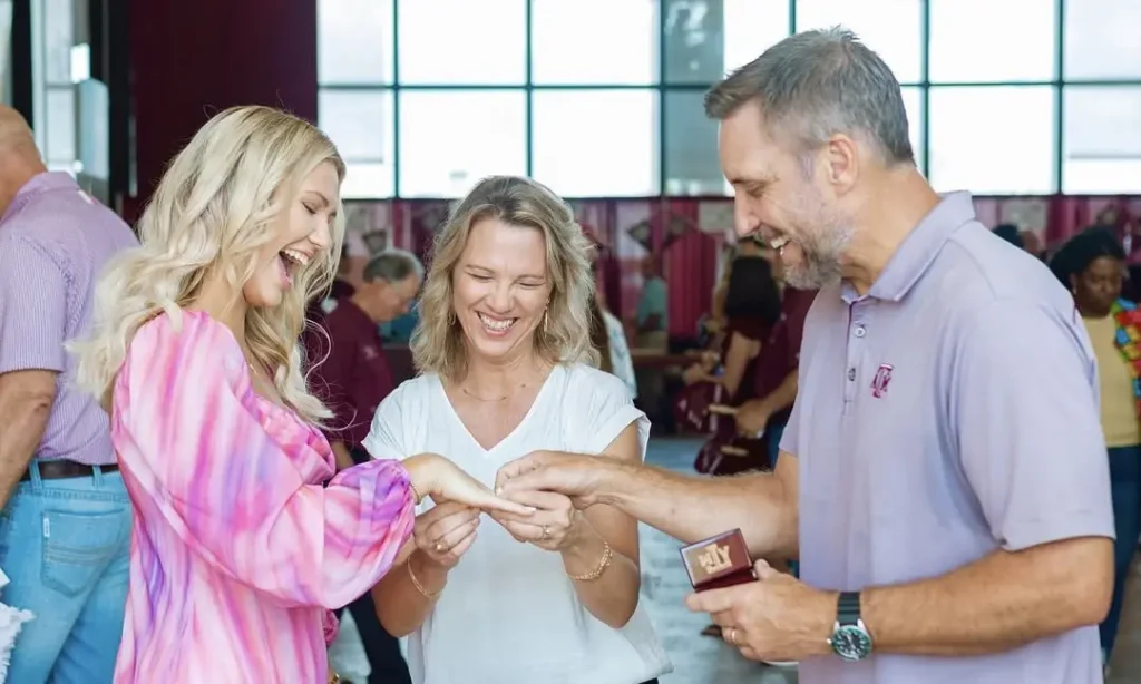 Aggie Graduate smiling with her parents while getting her class ring and RW Fine RingWrap at the baseball field