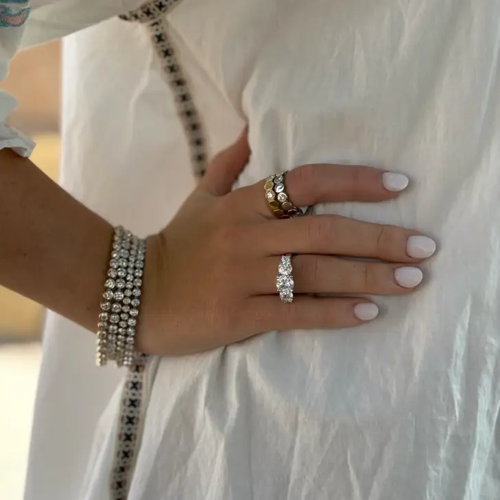 Womans hand with a three stone ring and stacked rings and bracelets